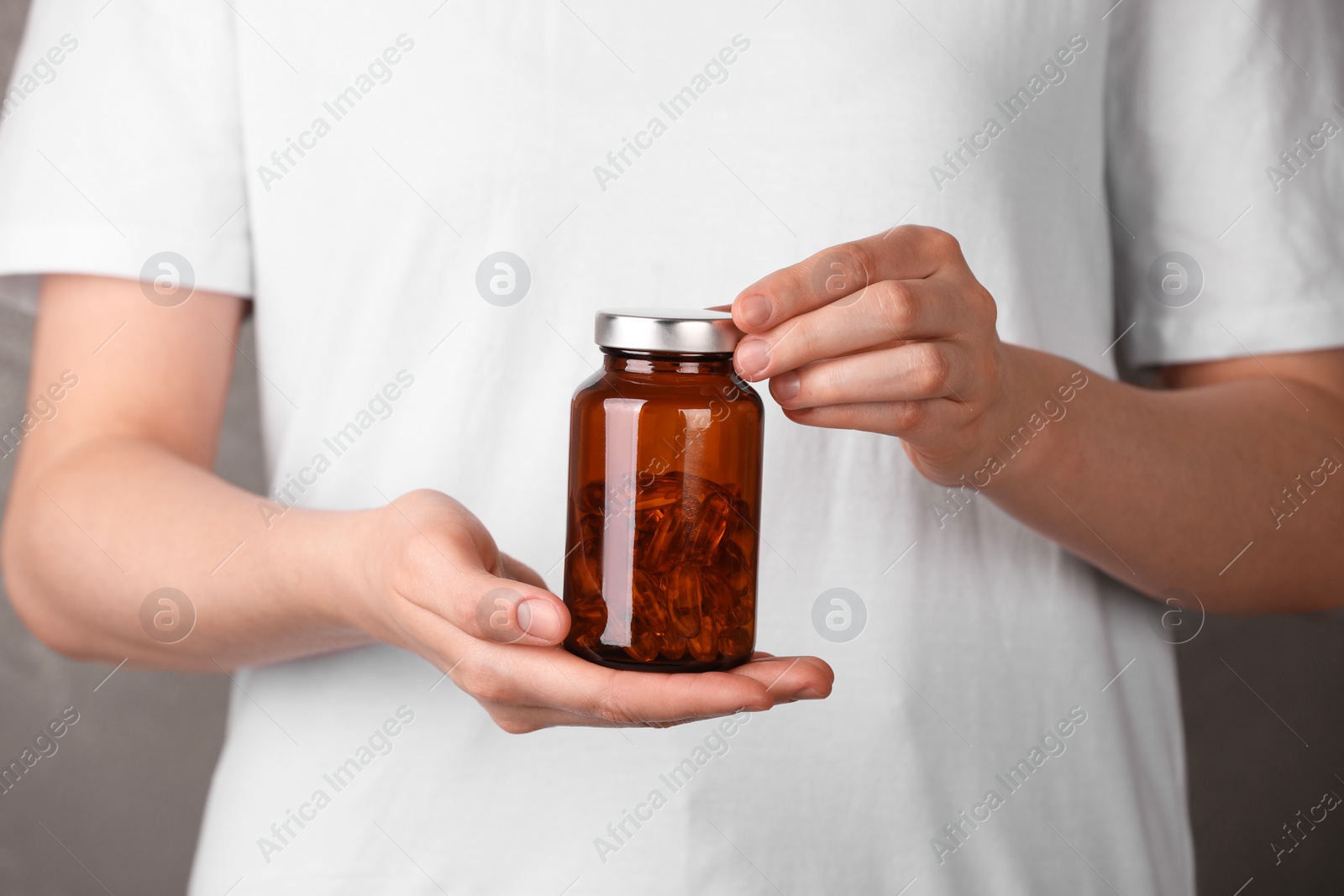 Photo of Woman holding bottle with vitamin capsules against light brown background, closeup