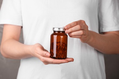 Woman holding bottle with vitamin capsules against light brown background, closeup