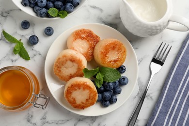 Delicious cottage cheese pancakes with blueberries, honey and mint on white marble table, flat lay