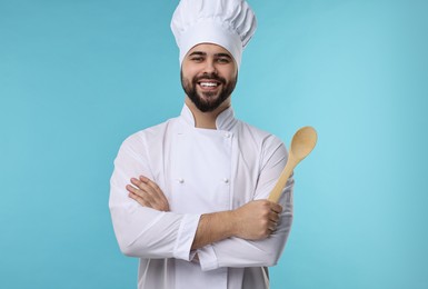 Photo of Happy young chef in uniform holding wooden spoon on light blue background