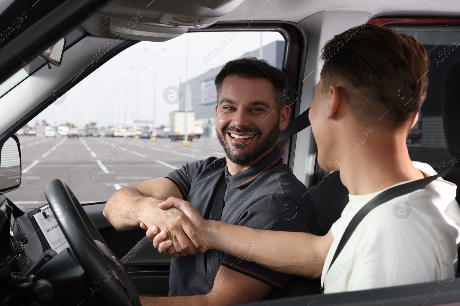 Photo of Driving school. Happy student shaking hands with driving instructor during lesson in car at parking lot