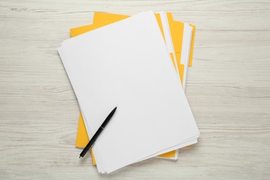 Yellow files with blank sheets of paper and pen on white wooden table, top view. Space for design