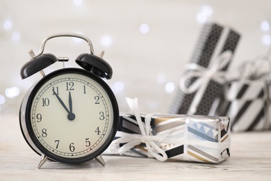 Vintage alarm clock with decor on white wooden table against blurred Christmas lights, closeup. New Year countdown