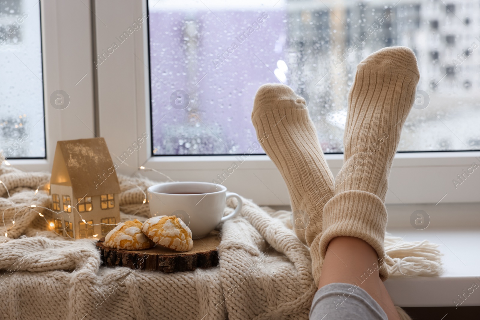 Photo of Woman in knitted socks relaxing near window at home, closeup. Space for text