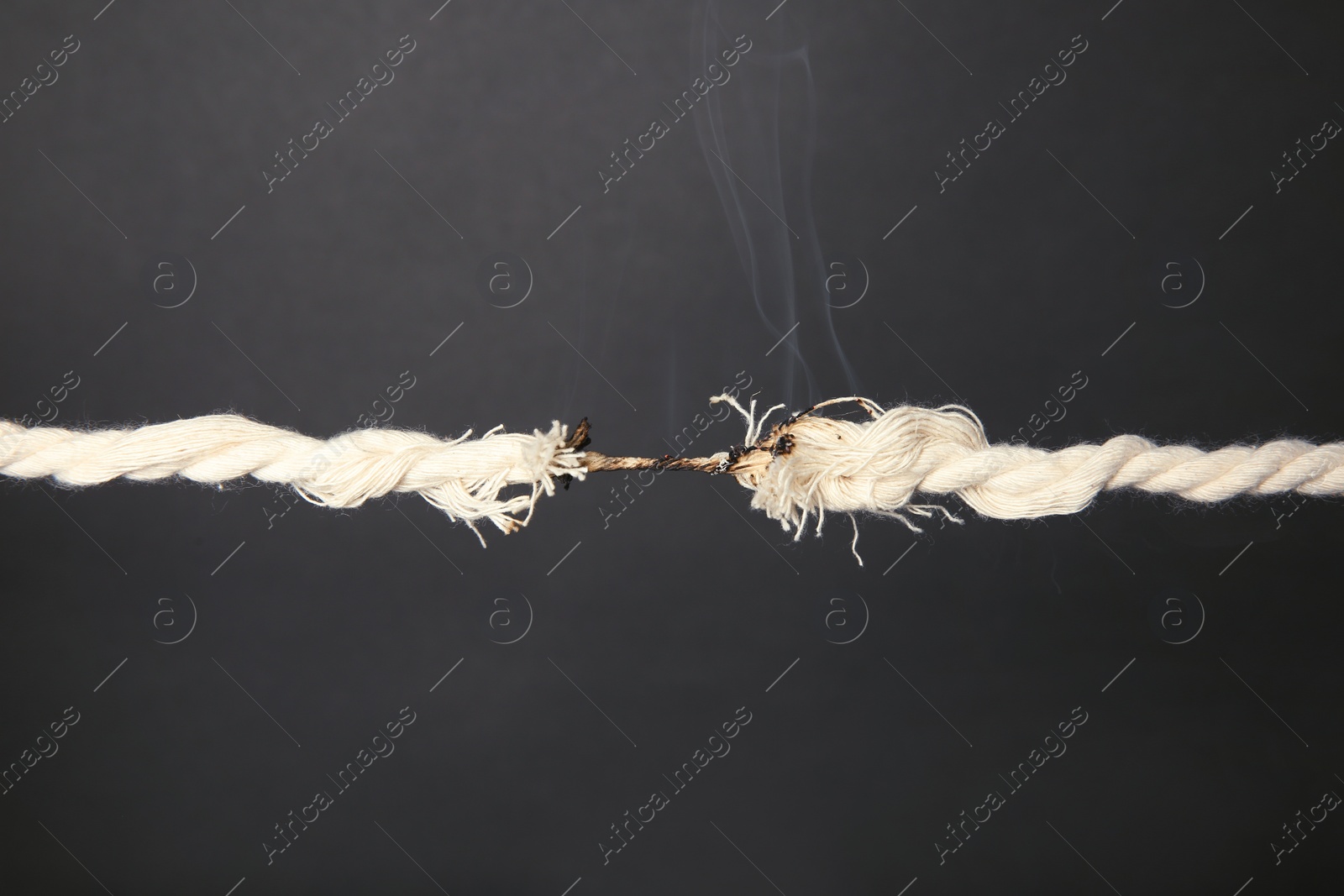Photo of Burning frayed rope at breaking point on gray background