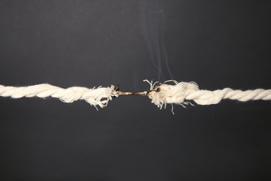 Burning frayed rope at breaking point on gray background