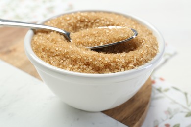 Photo of Brown sugar in bowl and spoon on table, closeup