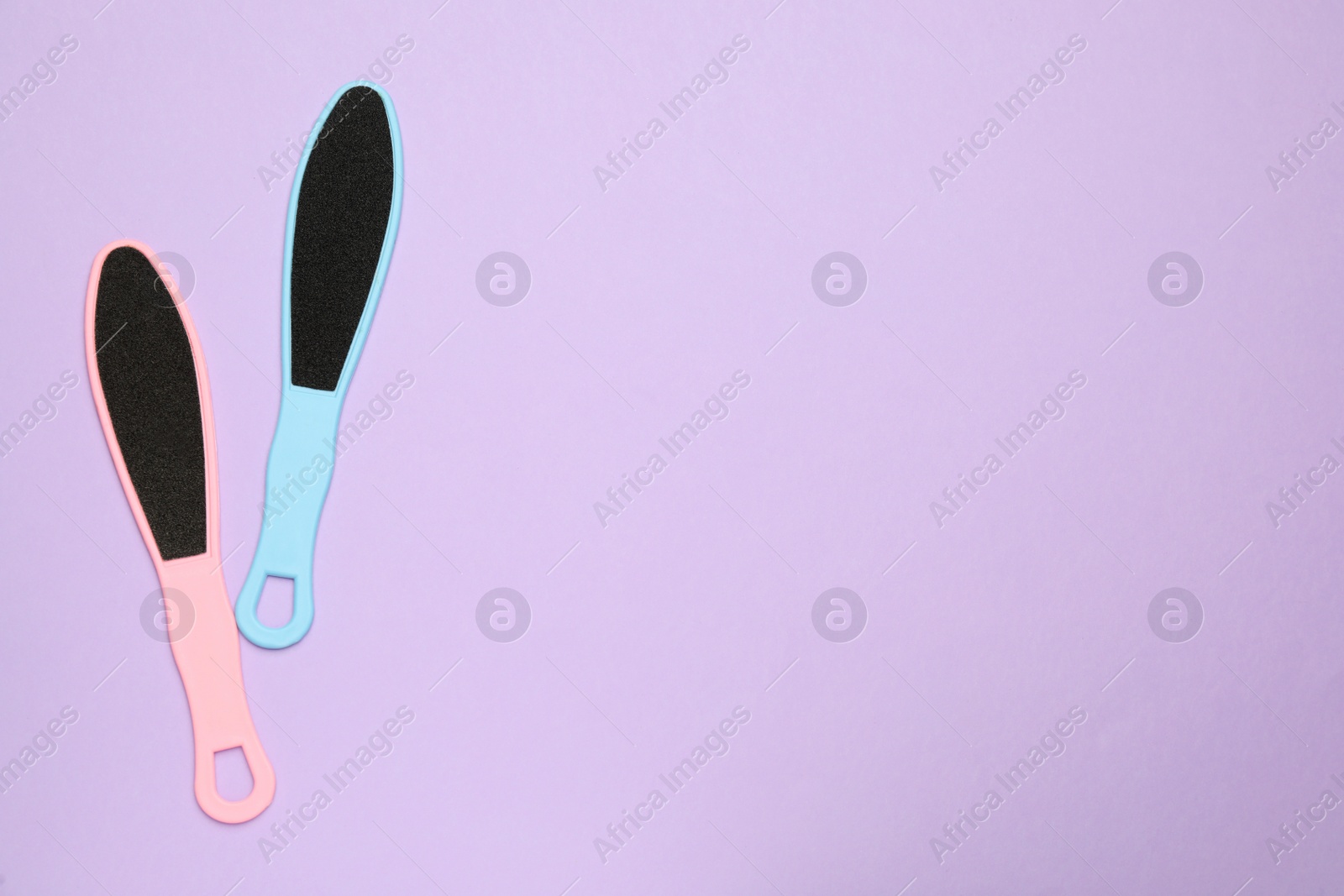 Photo of Colorful foot files on violet background, flat lay with space for text. Pedicure tools