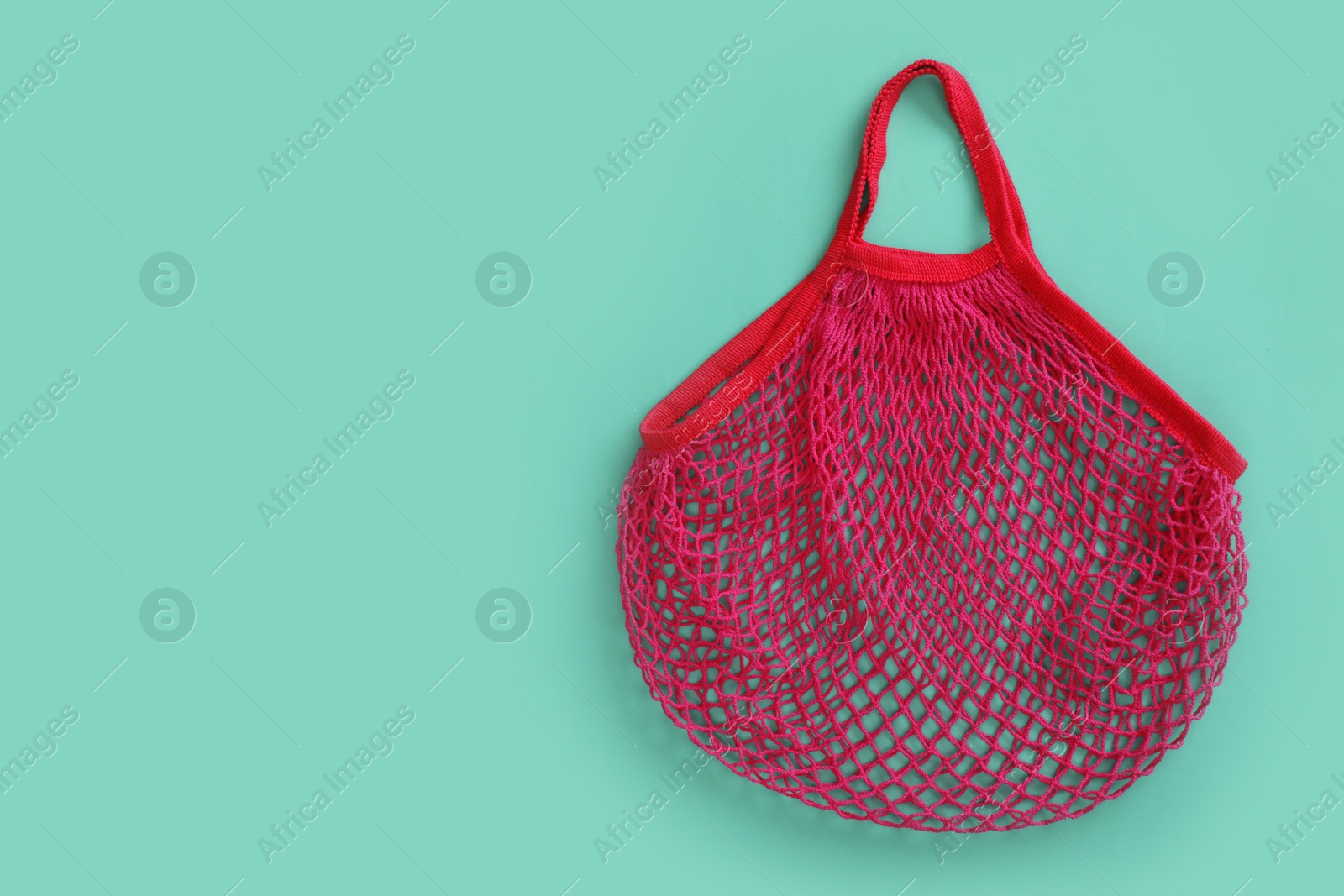 Photo of Empty net bag on turquoise background, top view. Space for text