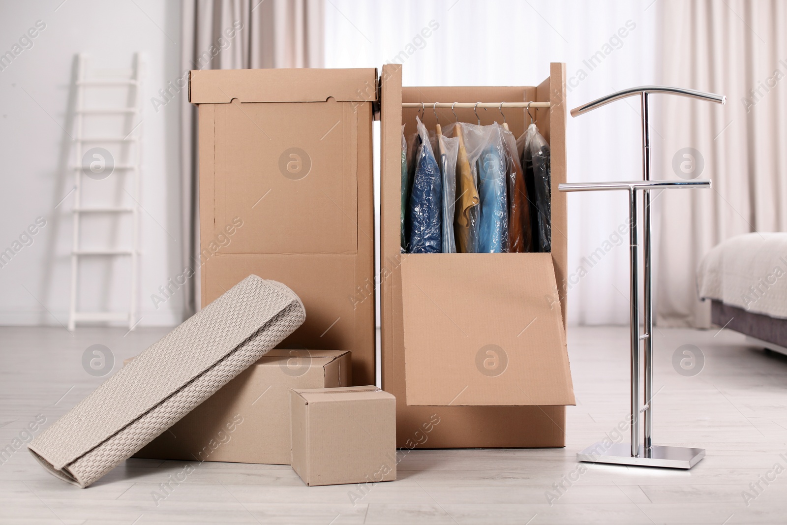 Photo of Cardboard wardrobe boxes with clothes on hangers and carpet indoors. Moving day