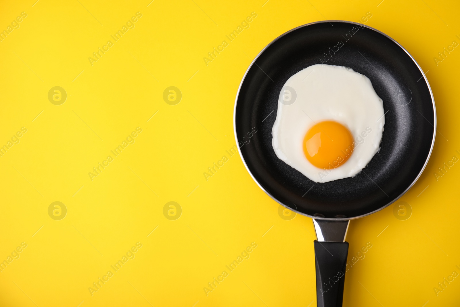 Photo of Tasty fried egg in pan on yellow background, top view. Space for text