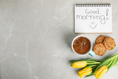 Photo of Delicious coffee, cookies, flowers and GOOD MORNING wish on grey table, flat lay. Space for text