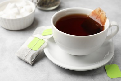 Photo of Tea bags and cup of hot beverage on light table, closeup