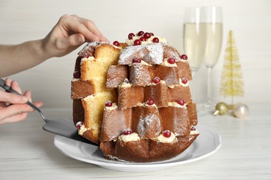 Woman taking slice of delicious Pandoro Christmas tree cake with powdered sugar and berries at white wooden table, closeup