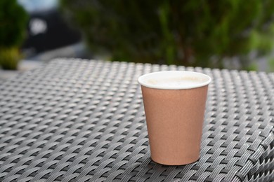 Photo of Coffee cardboard cup on rattan table outdoors, space for text