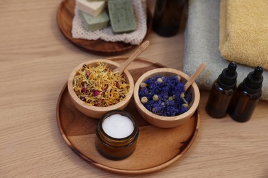 Photo of Dry flowers, bottles of essential oils and jar with cream on wooden table, above view. Spa time