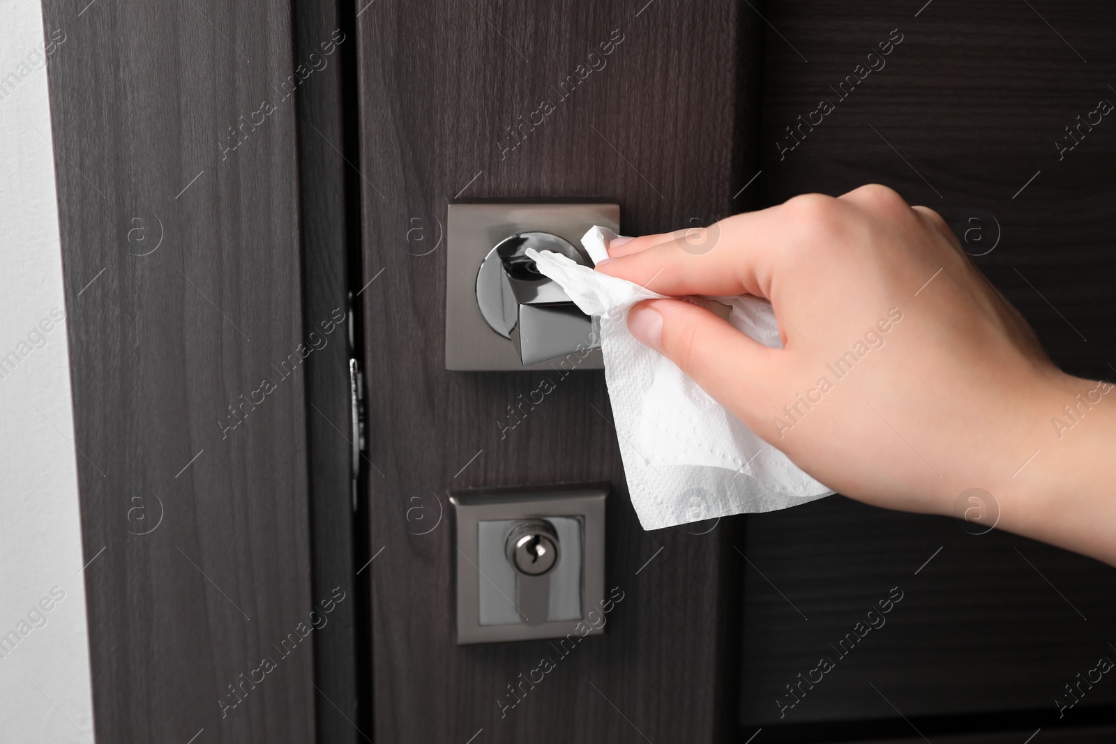 Photo of Woman cleaning door handle with paper towel indoors, closeup