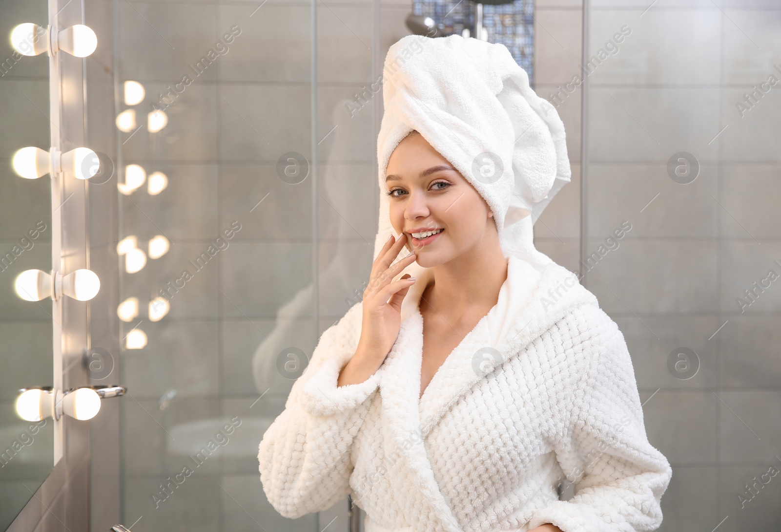 Photo of Beautiful woman with towel on head near mirror in bathroom