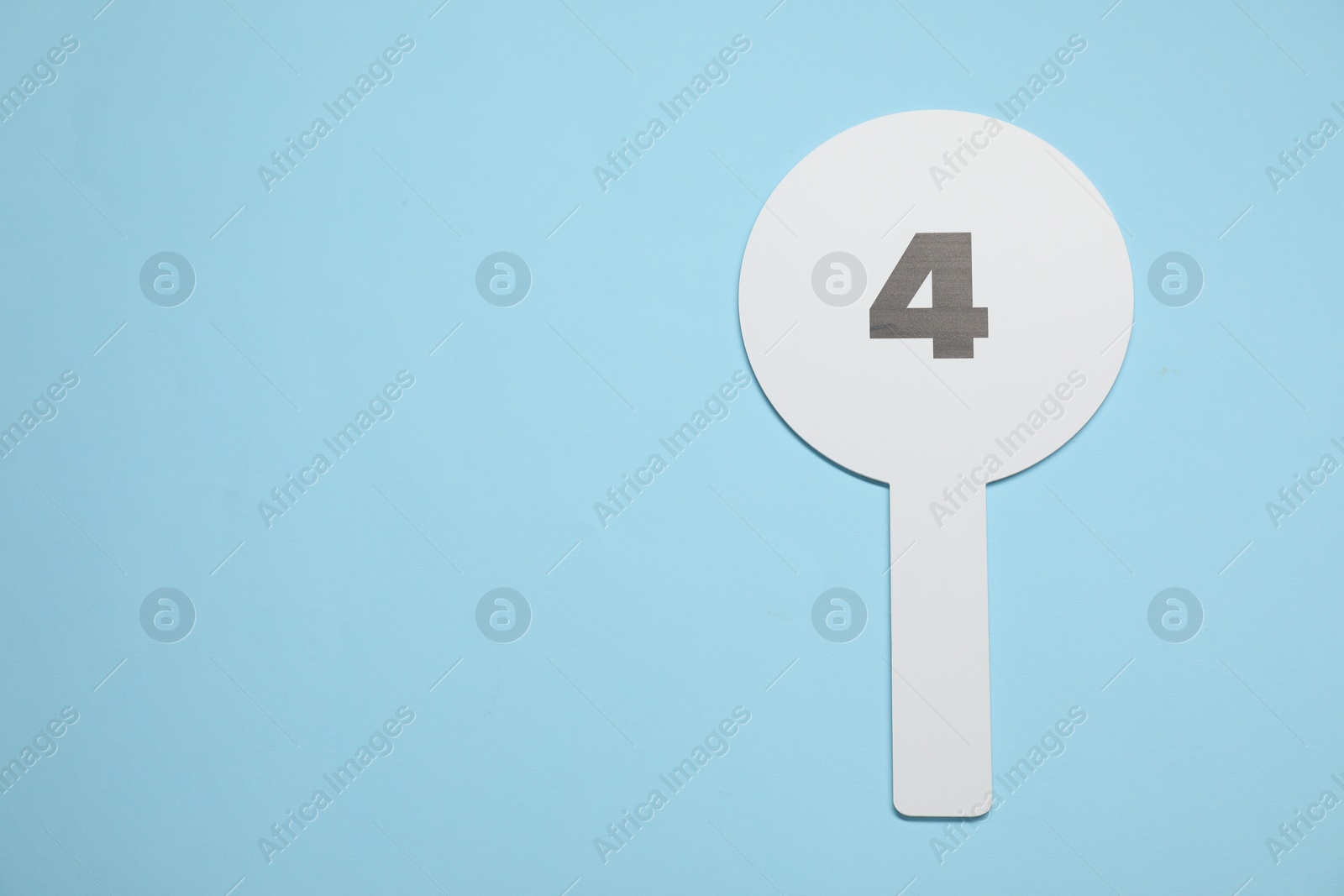 Photo of Auction paddle with number 4 on light blue background, top view. Space for text