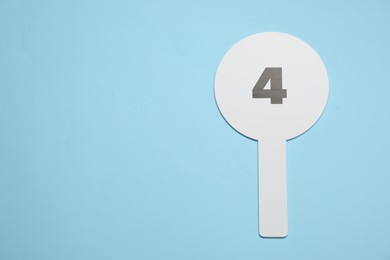 Auction paddle with number 4 on light blue background, top view. Space for text