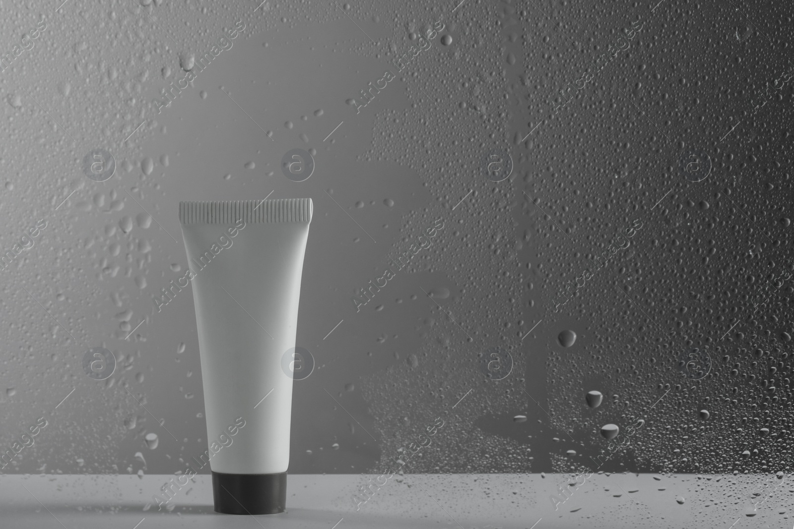 Photo of Tube with moisturizing cream on grey background, view through wet glass. Space for text