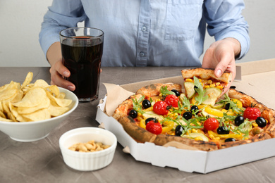 Woman taking slice of delicious vegetable pizza at grey table, closeup