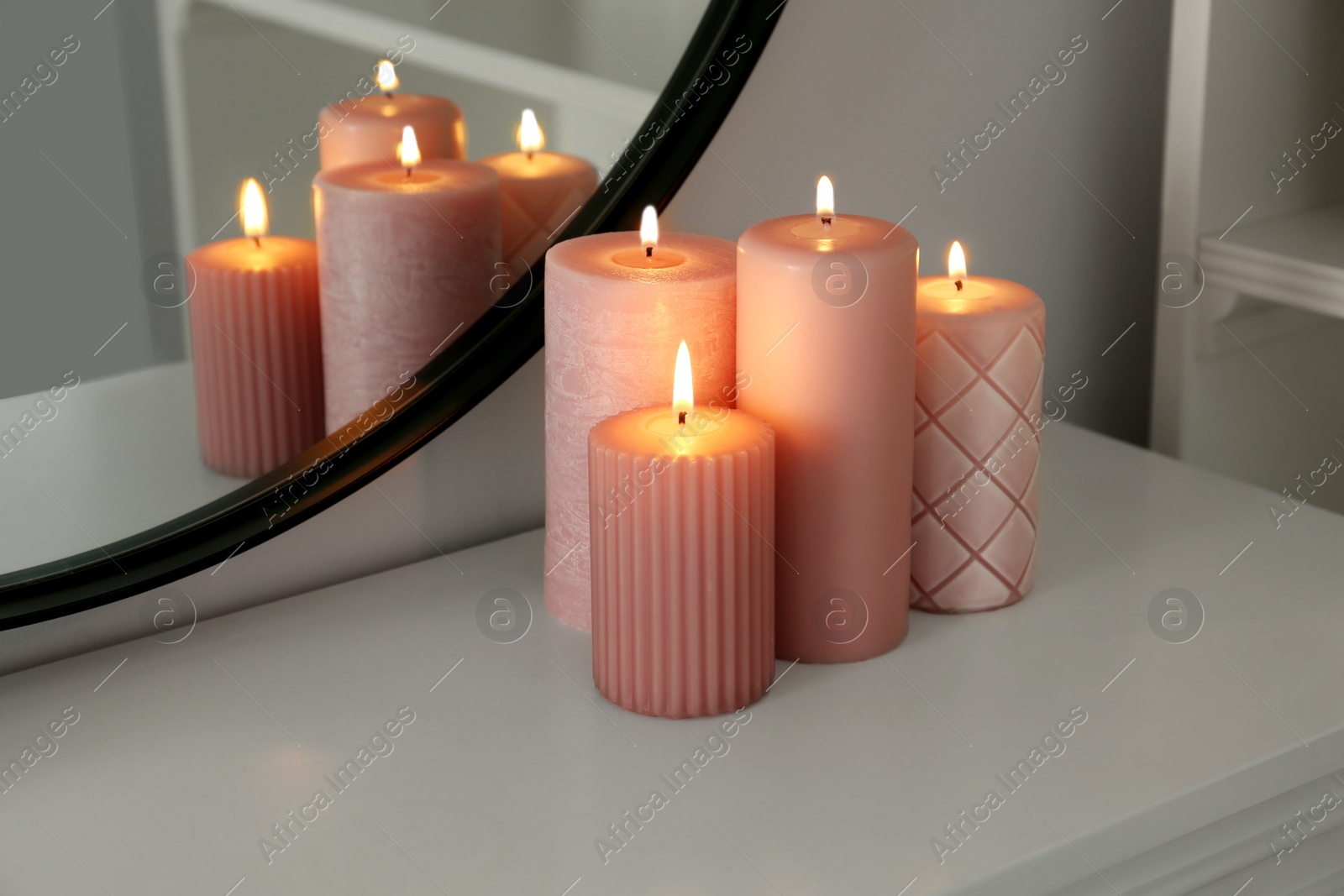 Photo of Beautiful burning candles on white console table near mirror indoors