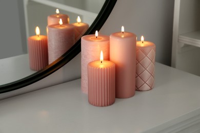 Beautiful burning candles on white console table near mirror indoors