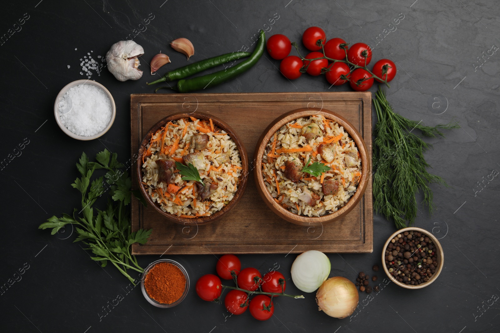 Photo of Delicious pilaf in bowls and products on black table, flat lay