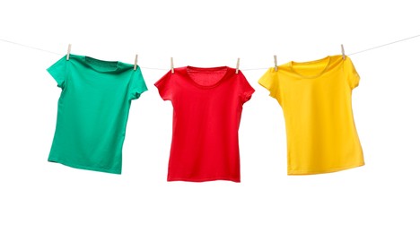 Different bright t-shirts drying on washing line against white background