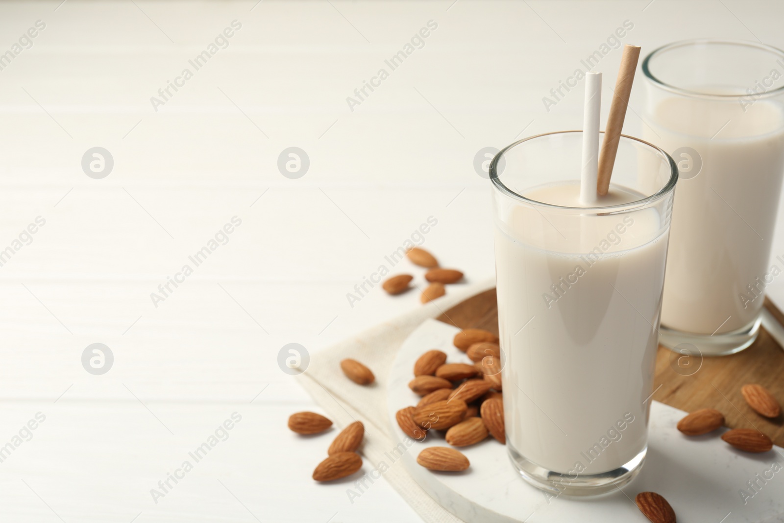 Photo of Glasses of almond milk and almonds on white wooden table, space for text