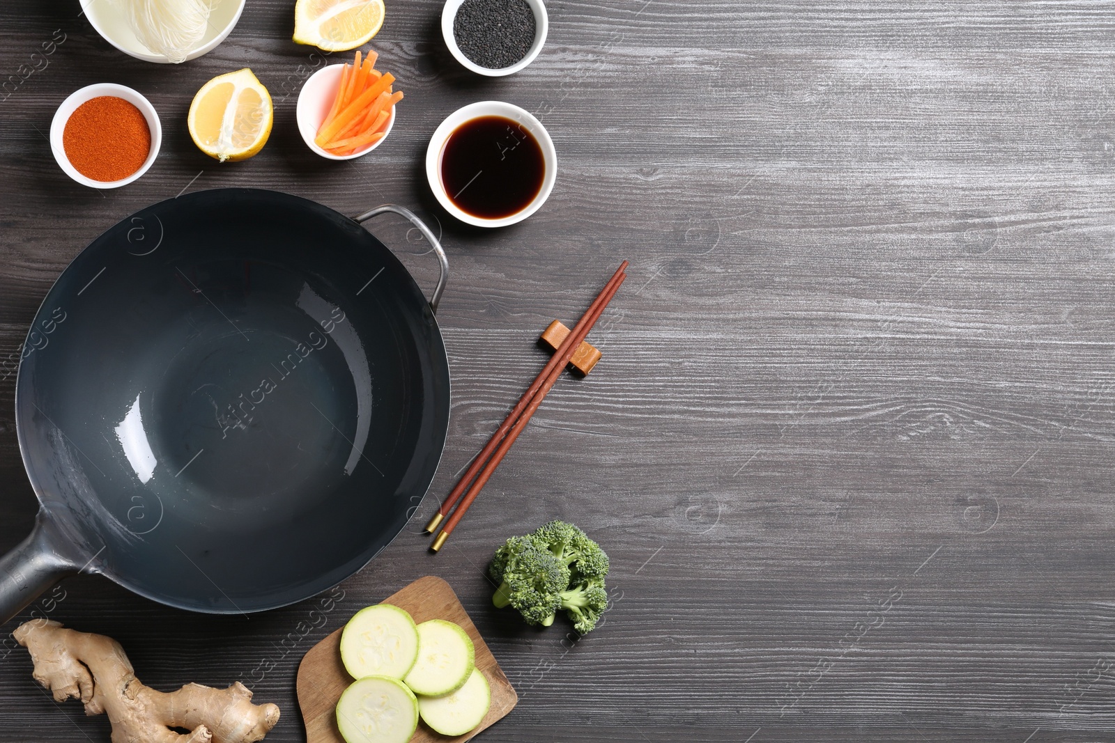 Photo of Empty iron wok, chopsticks and ingredients on grey wooden table, flat lay. Space for text