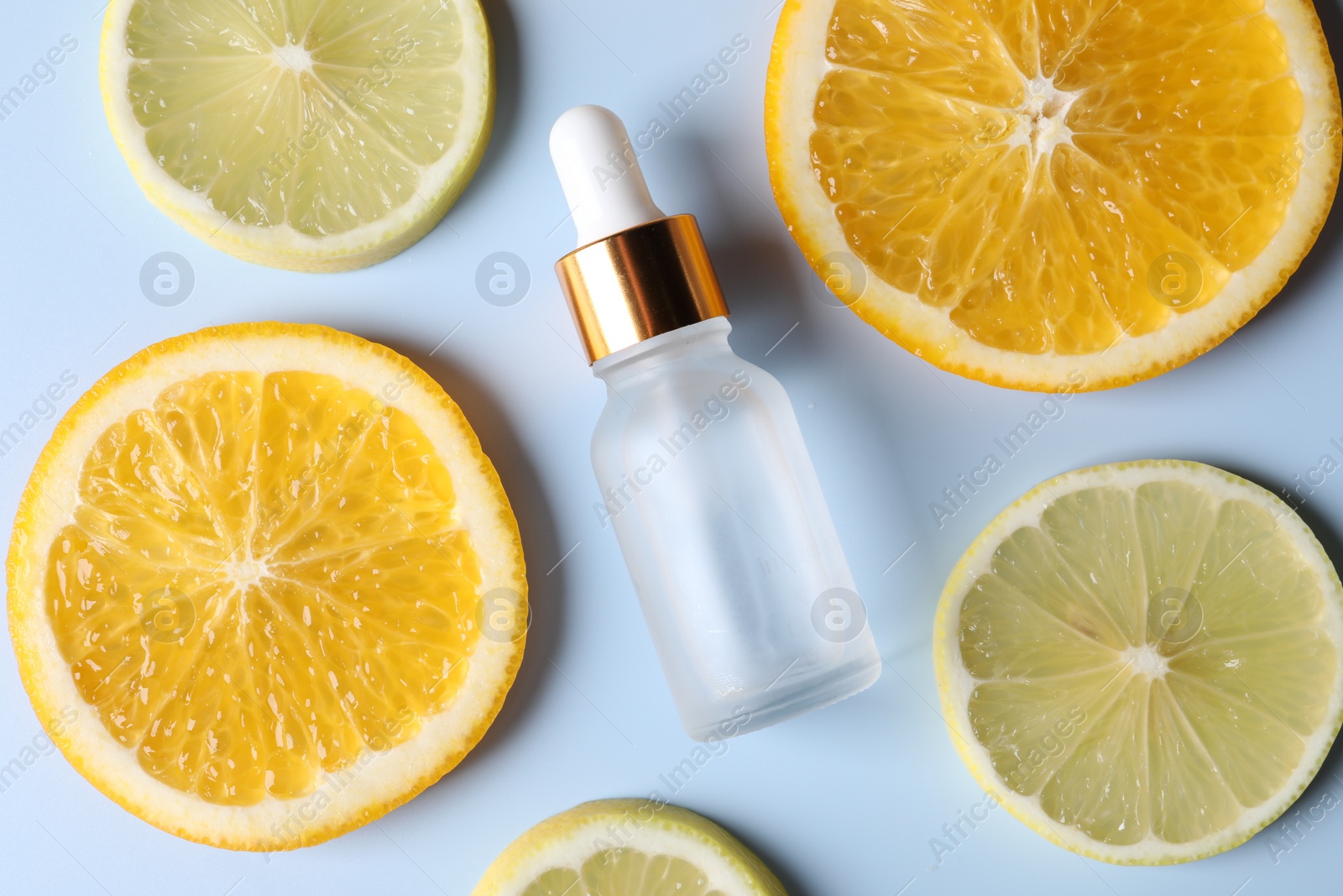 Photo of Bottle of cosmetic serum and sliced citrus fruits on light blue background, flat lay