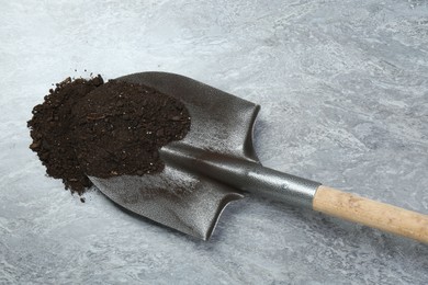 Photo of Metal shovel with fertile soil on gray textured surface, top view