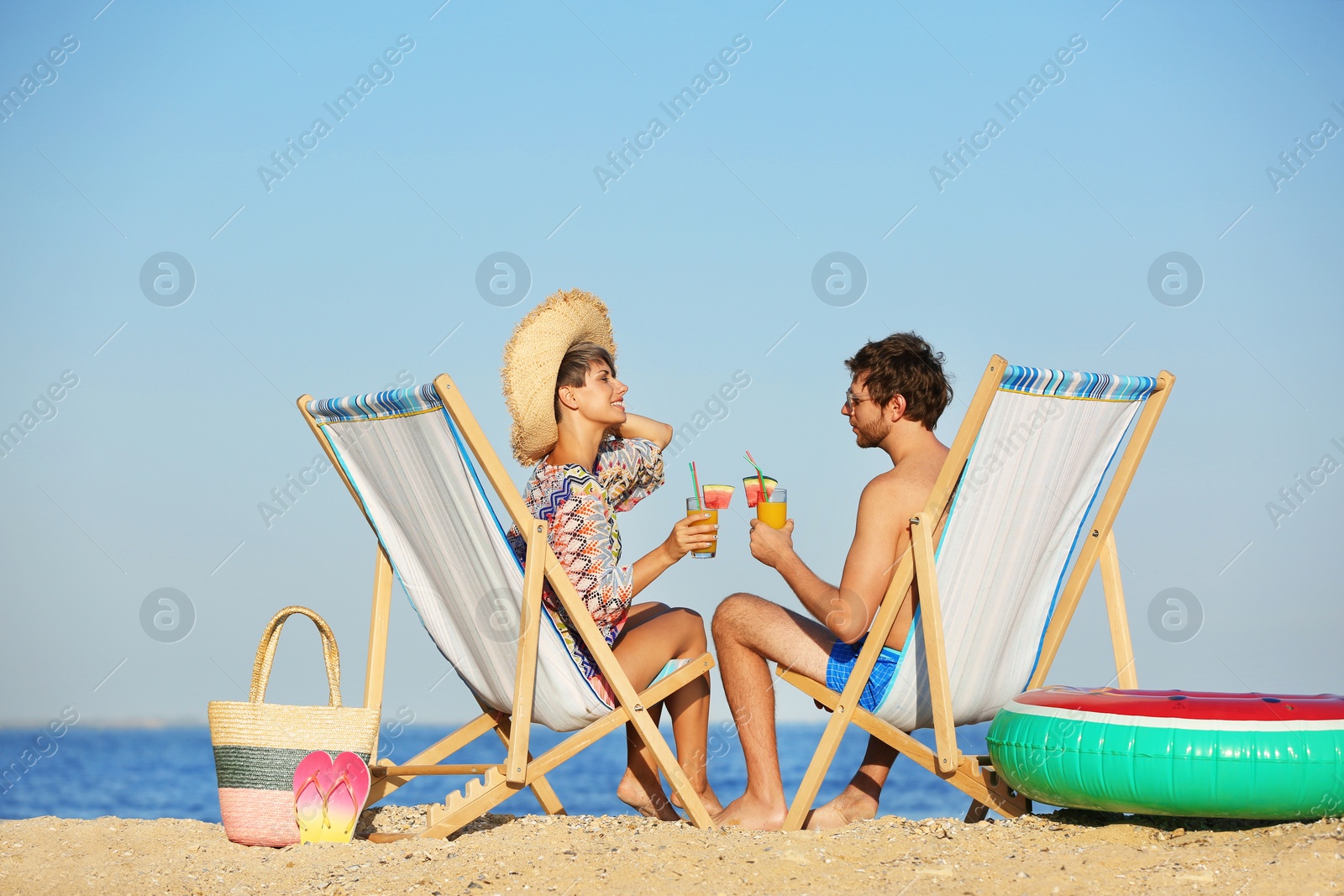 Photo of Young couple with cocktails in beach chairs at seacoast