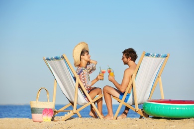 Young couple with cocktails in beach chairs at seacoast