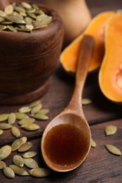 Photo of Spoon with oil and pumpkin seeds on wooden table
