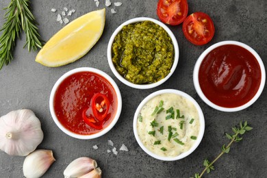 Different tasty sauces in bowls and ingredients on grey table, flat lay