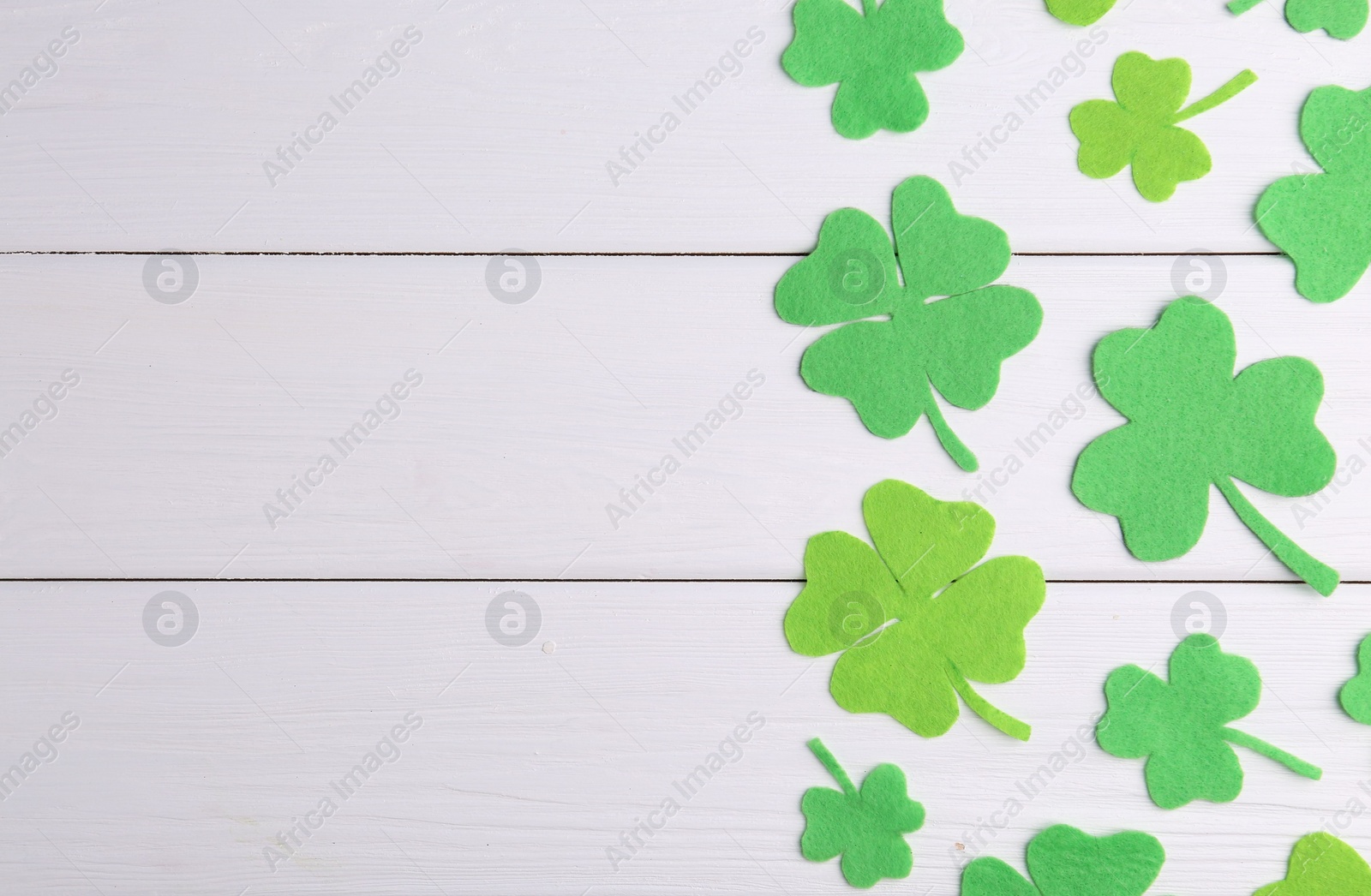 Photo of St. Patrick's day. Decorative green clover leaves on white wooden table, flat lay. Space for text