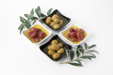 Photo of Bowls with different ripe olives and leaves on white background