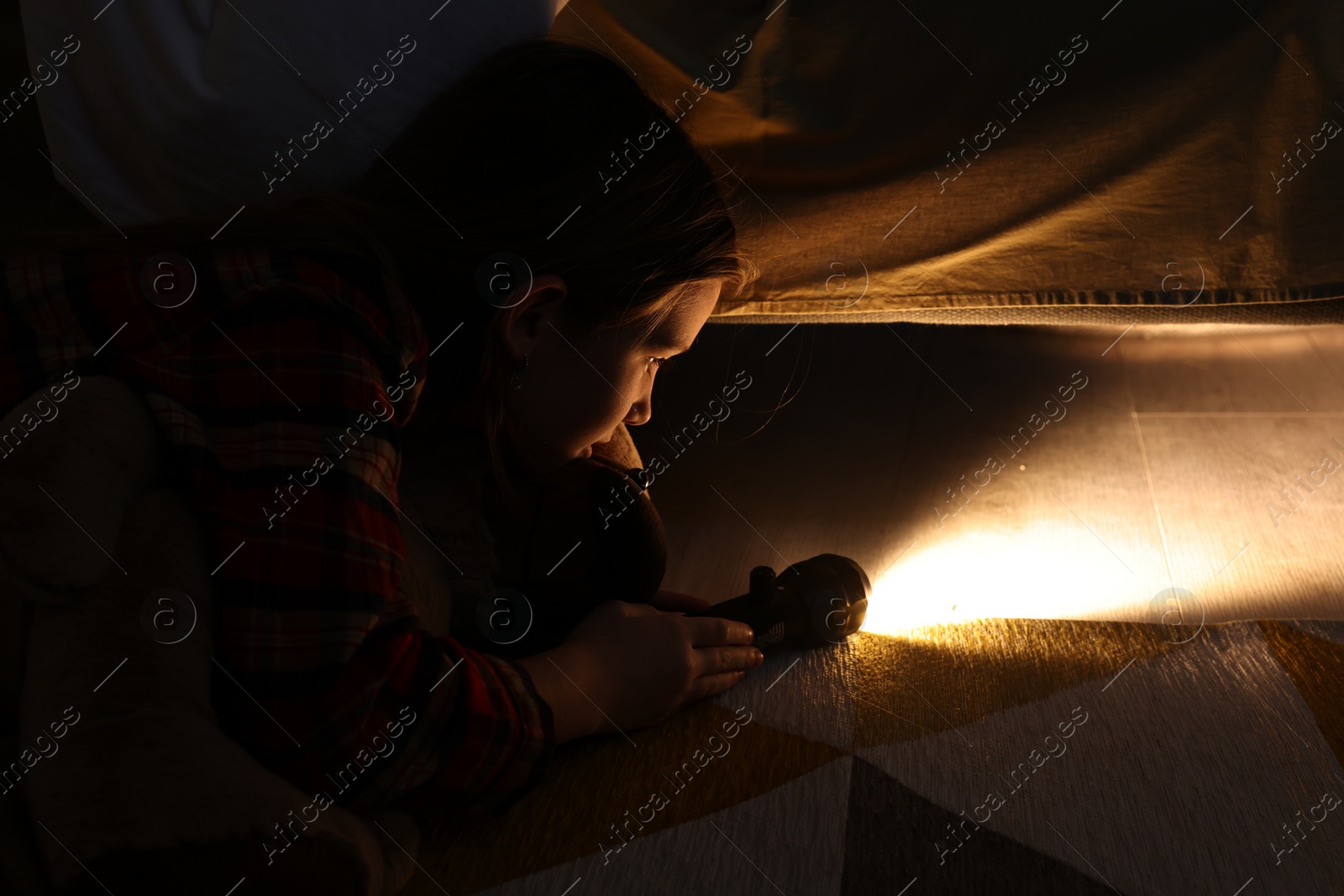 Photo of Little girl with flashlight looking for monster under bed at night