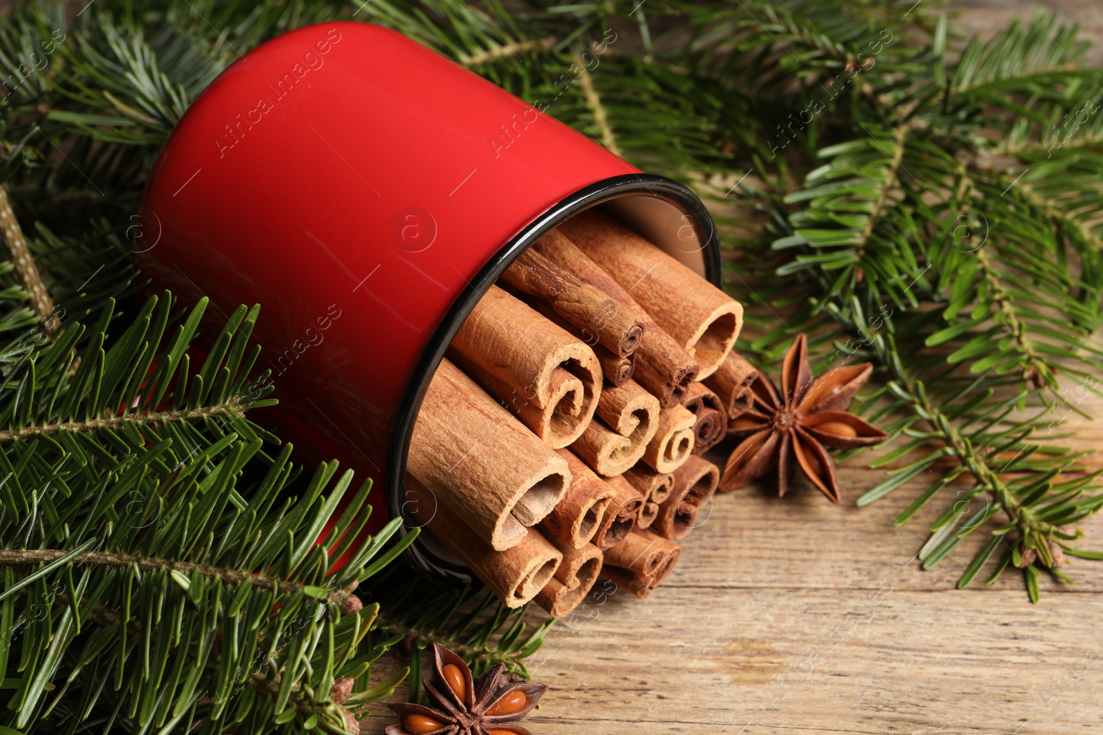 Photo of Many cinnamon sticks, anise stars and fir branches on wooden table, closeup. Aromatic spices