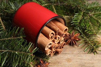 Many cinnamon sticks, anise stars and fir branches on wooden table, closeup. Aromatic spices