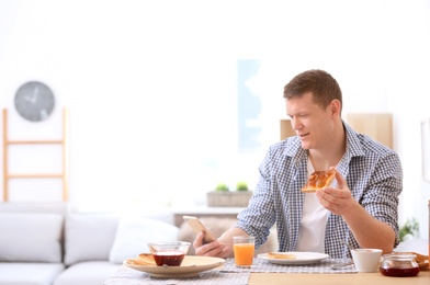 Photo of Young man eating tasty toasted bread with jam at table