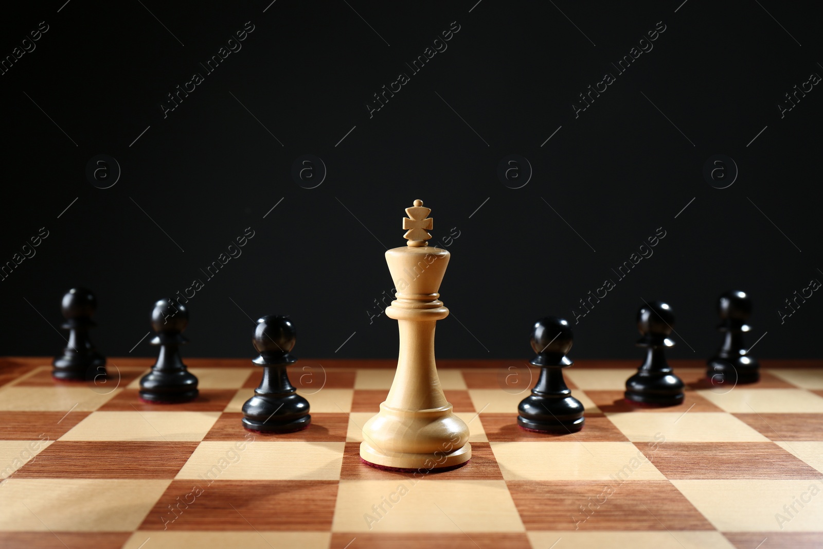 Photo of White king among black pawns on wooden chess board against dark background