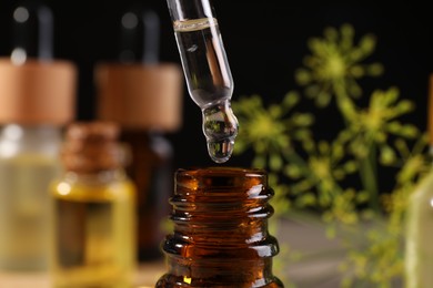 Dripping dill essential oil from pipette into bottle on blurred background, closeup