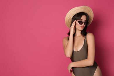 Beautiful young woman wearing swimsuit, hat and sunglasses on pink background. Space for text