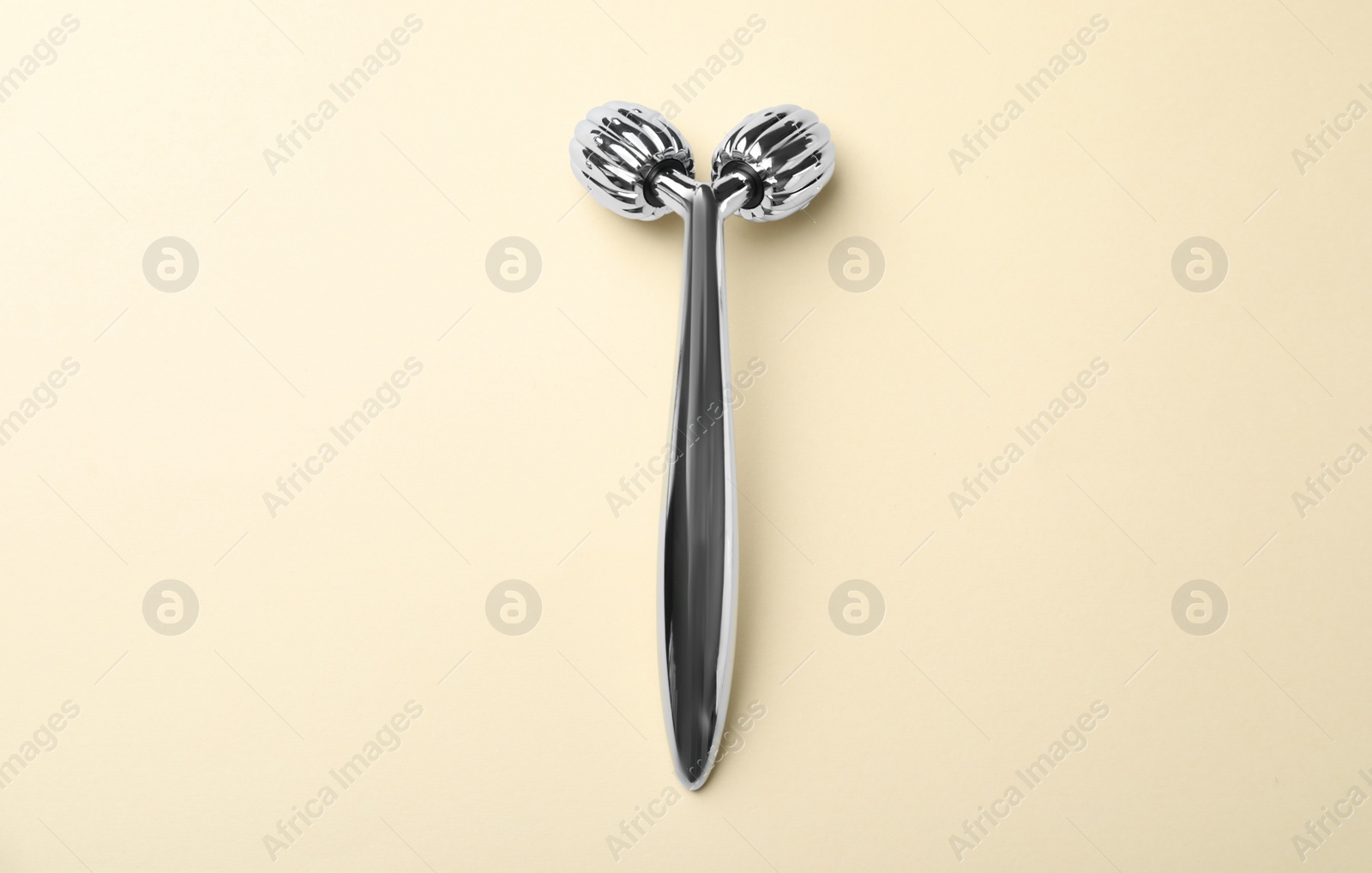 Photo of Metal face roller on beige background, top view