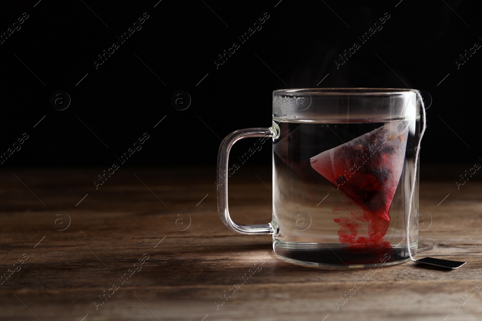 Photo of Tea bag in cup of hot water on wooden table. Space for text