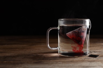 Tea bag in cup of hot water on wooden table. Space for text